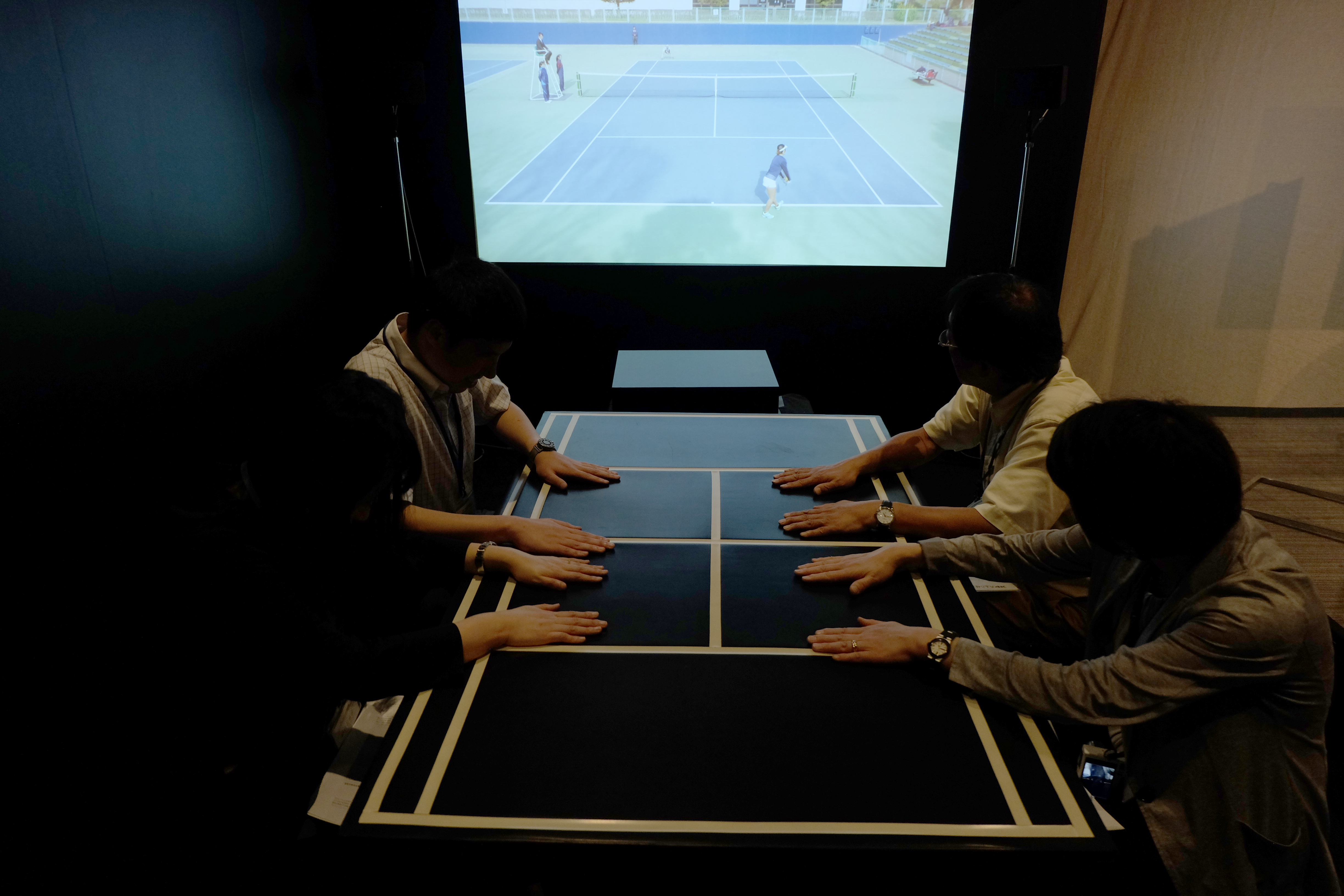 「暗闇で感じるテニス」の体験の様子。体験者は暗いブースの中で、最初は映像を見ながら、次に映像を消し、最後は振動のみでテニスの試合を体感する。